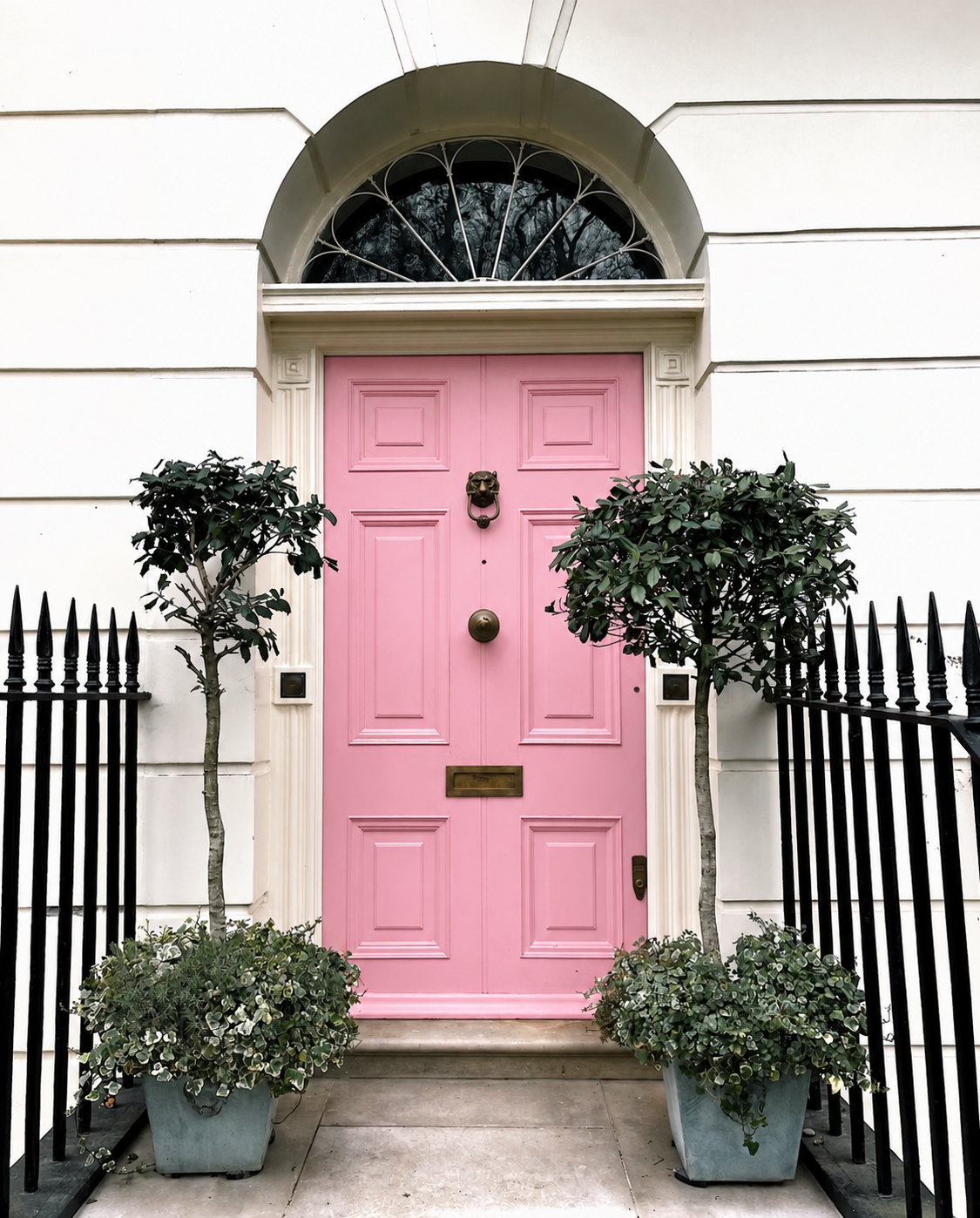 Pink front door framed by greenery and an ivory facade